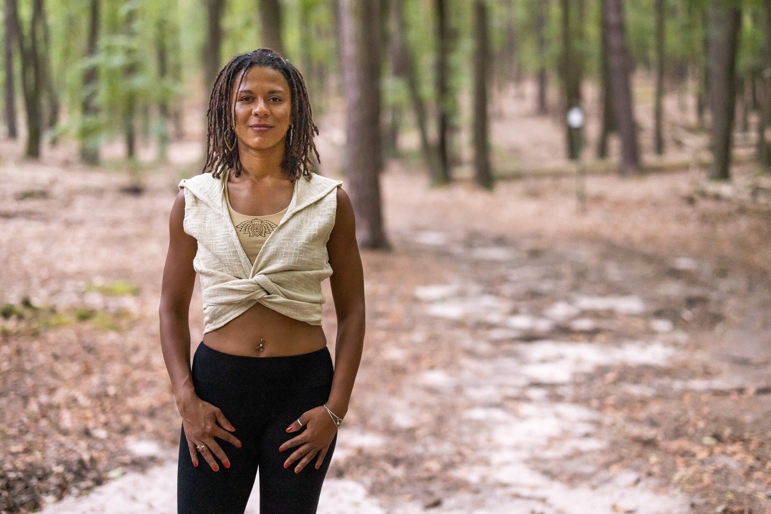 Woman standing in a forest wearing a sleeveless vest in off-white. It is a hooded vest in natural fabric and a piece of alternative clothing for women from Anna Suno brand for natural clothing. 