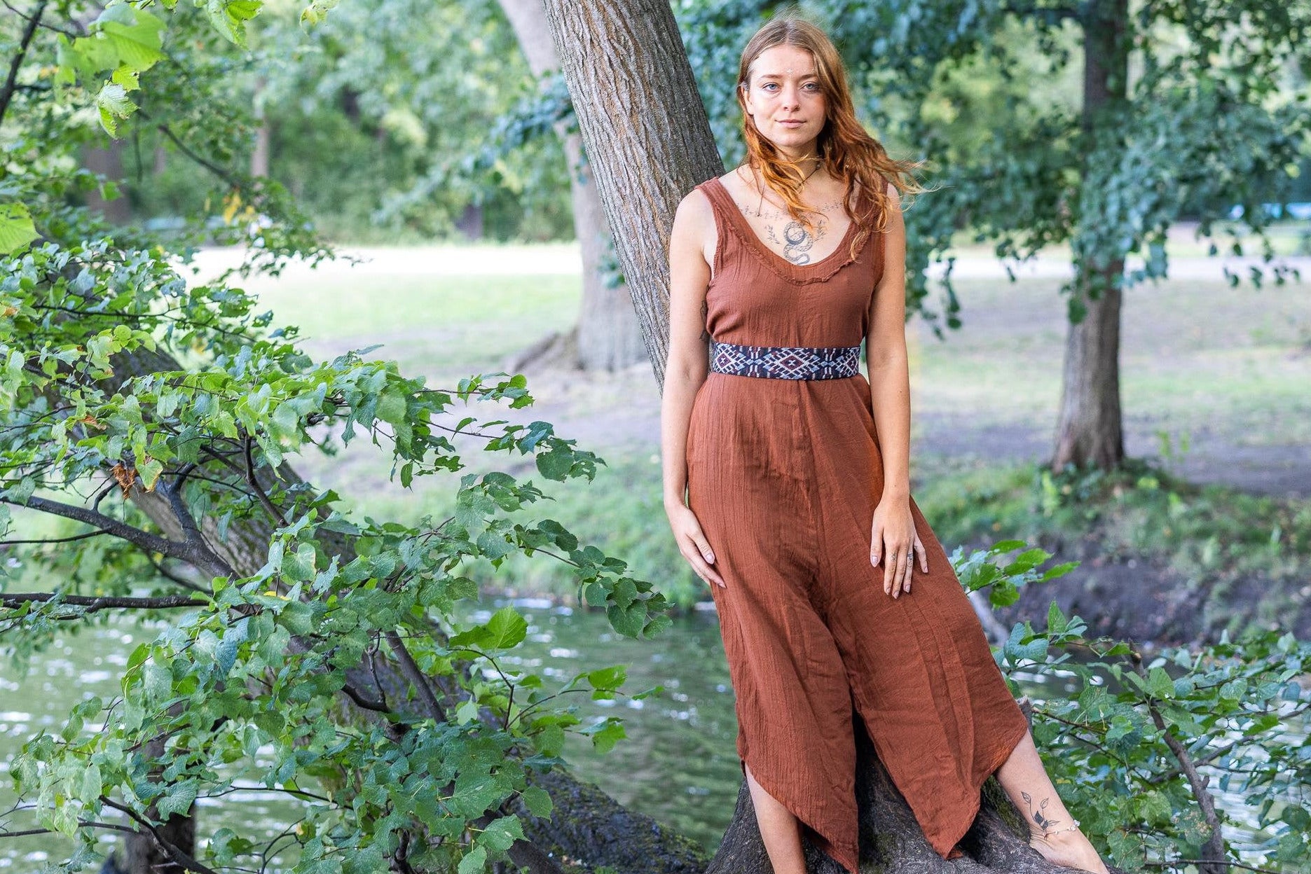 Woman in a rust-colored jumpsuit standing by a tree in a park